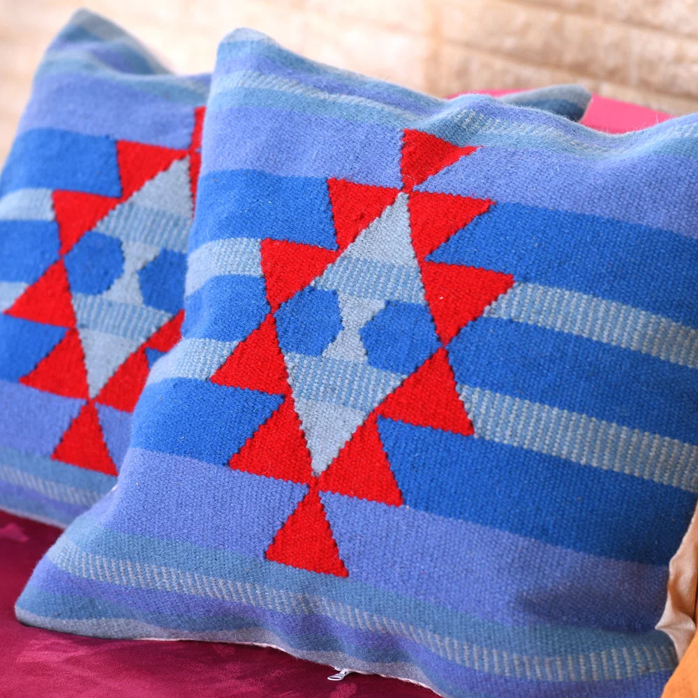 A detailed view of two vibrant square pillows, showcasing a design with blue vertical stripes and a prominent red geometric pattern, including triangles and diamonds, against a soft texture.