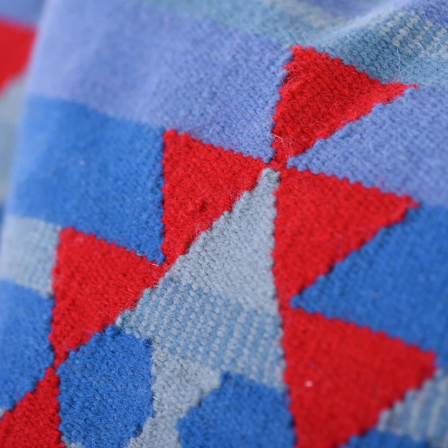 A close-up view of a decorative pillow featuring a geometric pattern in shades of red, blue, and light gray, highlighting the intricate texture and design details.