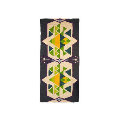 "A woven rug with geometric patterns in green, yellow, blue, and purple on a dark background, displayed vertically."