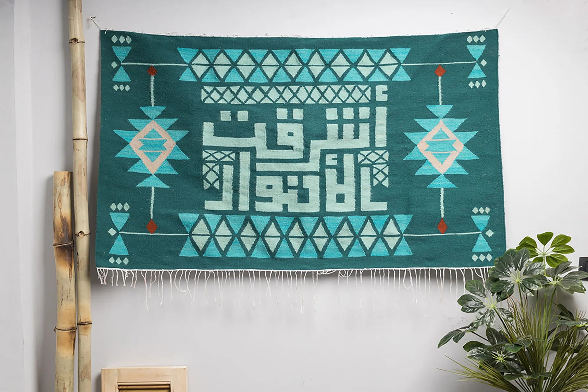 "A flat lay of a decorative wall hanging featuring Arabic calligraphy and geometric patterns in green and mint, with a wooden hanger at the top."