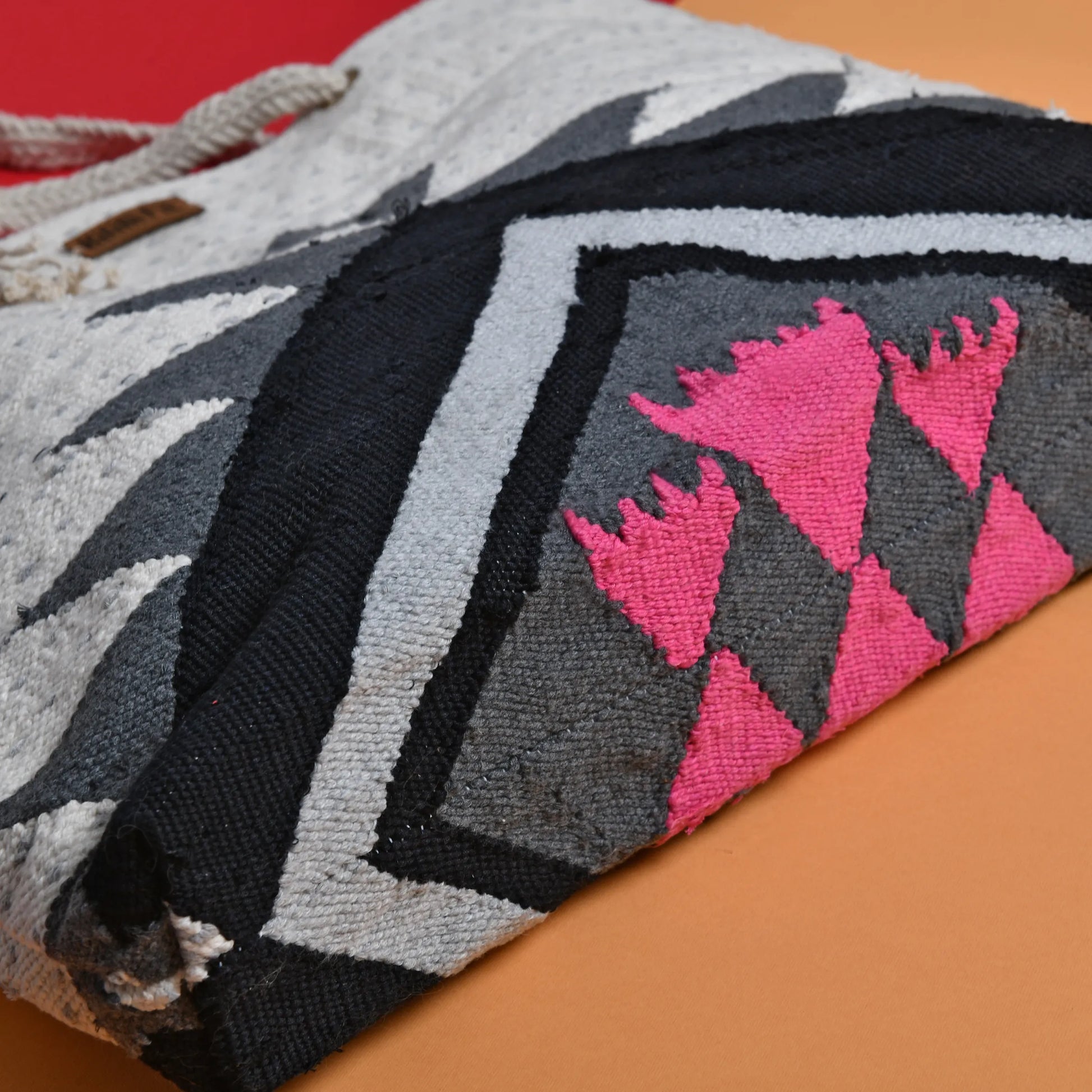 "Close-up of the geometric pattern on a handwoven tote bag, featuring black, gray, white, and pink colors."