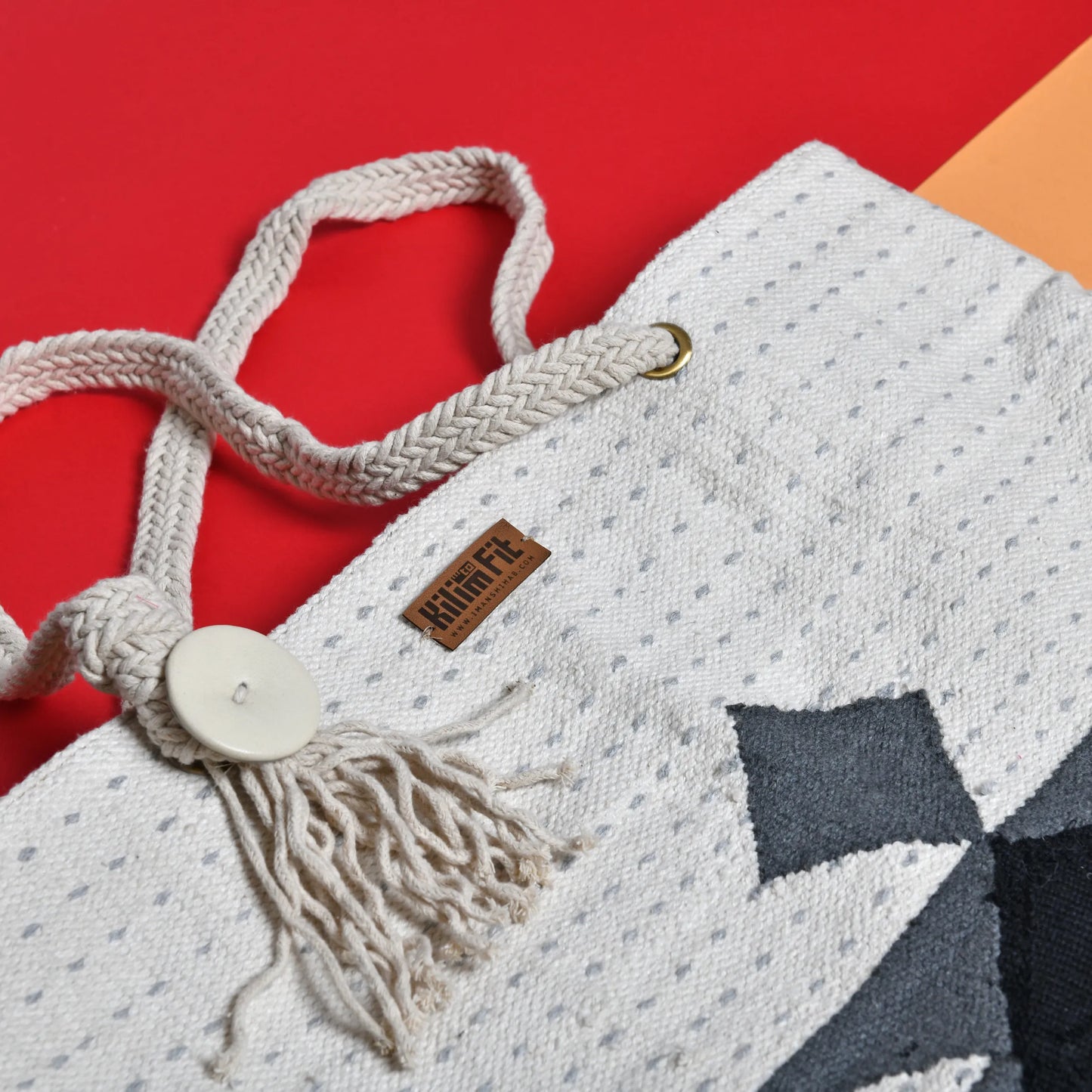 "Close-up of the top of a handwoven tote bag showing a button closure with a tassel and a label that reads 'Kufuf'."