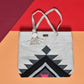 "A woven tote bag with a geometric pattern in black, white, and gray, placed on a colorful background, featuring a rope handle and a tassel."