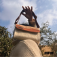 A person holds a woven handbag up against a cloudy sky. The bag features a terracotta and cream design with a textured pattern and a brown leather strap. The person's cozy sweater adds warmth to the composition, while the brand tag "KUFUF" is visible, emphasizing the bag's stylish appeal.
